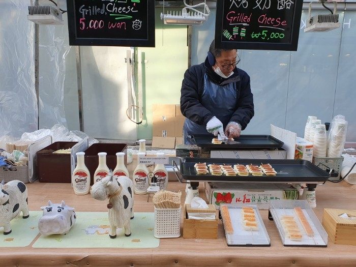 チーズと餅を串に刺して焼いた串焼き1本5000ウォン。注文すると、焼いた串焼きを紙コップに入れ練乳をかけてくれる。