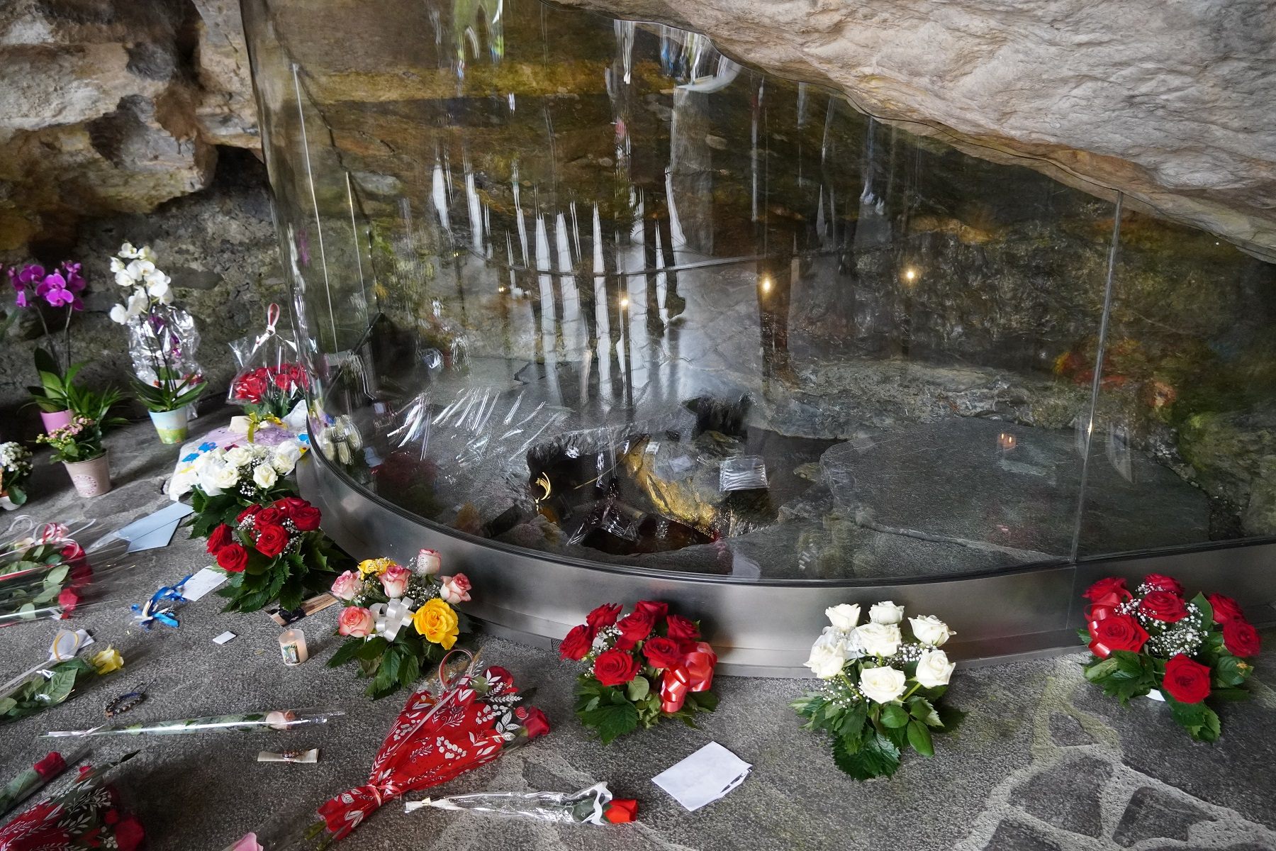 ガラスの囲いで覆われた奇跡の泉の前にはたくさんの花が手向けられている