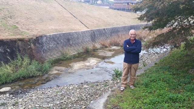 47年前の豪雨で氾濫した厚東川の河原で、防災対策の必要性を話す境憲一さん＝山口県宇部市で